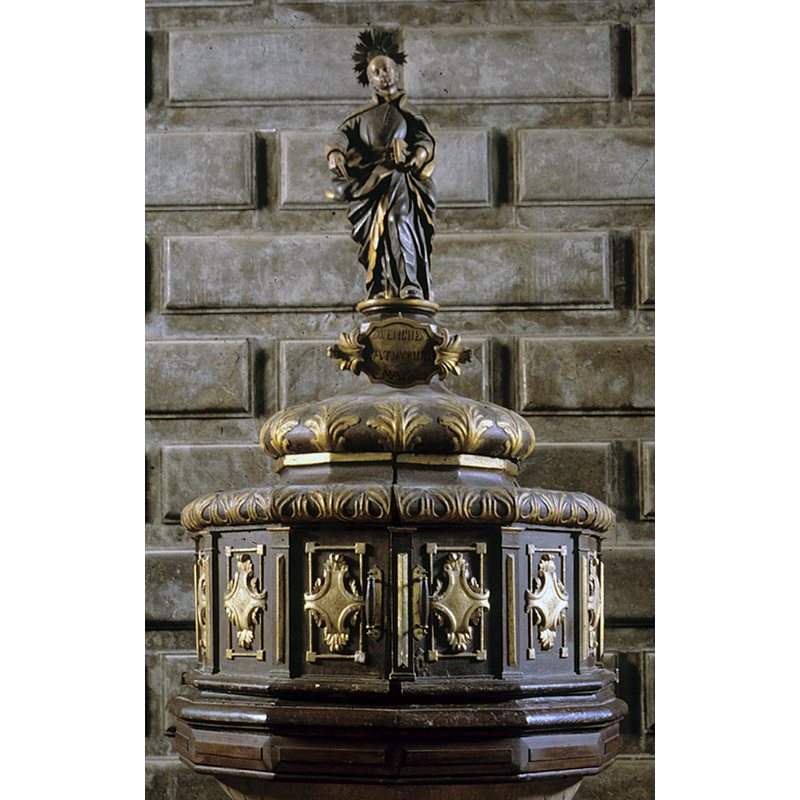 wooden cover of the rim-buffet type, but almost a canopy as the bottom of the cover hides practically 2/3 of the basin; the finial is a statue of St Ignatius of Loyola, who is supposed to have been baptised in this font