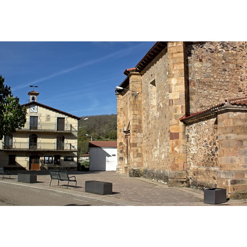 the church partially visible on the right, in the context of the village square; the town hall partially visible back, on the centre-left