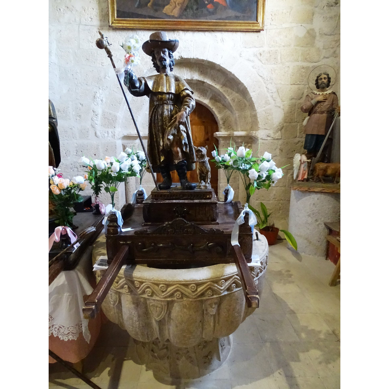 the wooden object on the font is not a font cover, but a float; the statue must be St. Roch, identified in the Golden Legend; became very popular during the plagues all over Europe; usually depicted showing his leg wounds, which a dog would lick to healing -- very dapper here in his 'French' hat here