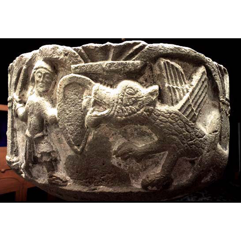 A warrior, carrying a long pointed shield, holding a sword in his right hand fights a winged dragon