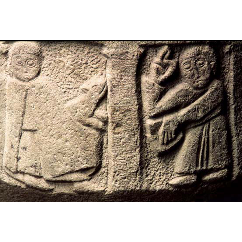 the scene spread over two arches: on the left a caped figure with a small animal that faces right; on the right a cleric holds an open book in the left arm and raises the right in benediction
