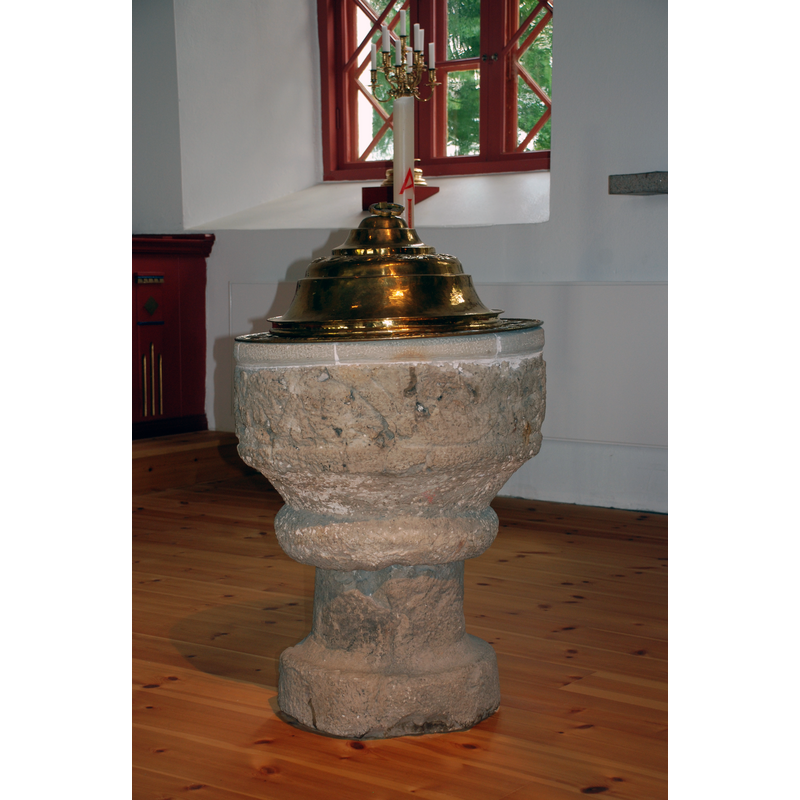 inside the new church inaugurated in 1866; the font has been repaired but most of the carving relief has been lost -- see the 1891 photograph by Sanfrid Welin [Image no.: 0200930001] for the decoration on the basin sides -- the font uses now both a baptismal dish and a low-dome cover, both apparently made of brass