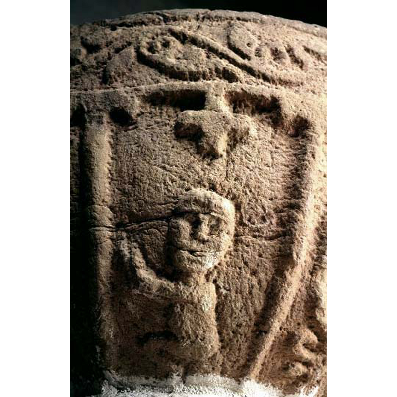 the figure appears to be seating (or crouching?), hands raised; the body is in profile but the head faces out; small Greek cross above