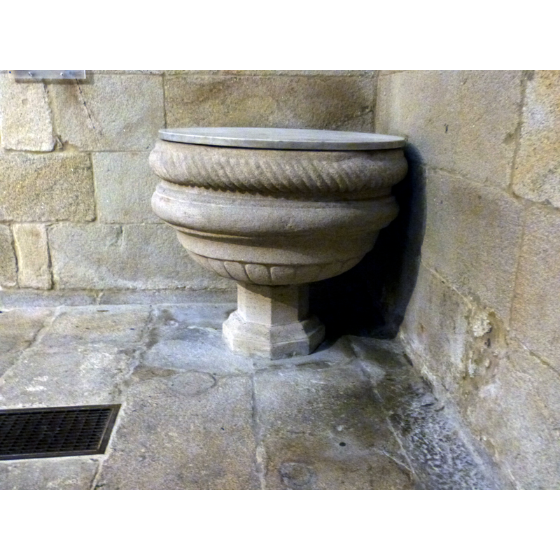 a modern font in the cathedral; it is located in a corner between the tower entranceway (on the left) and the north aisle (on the right)