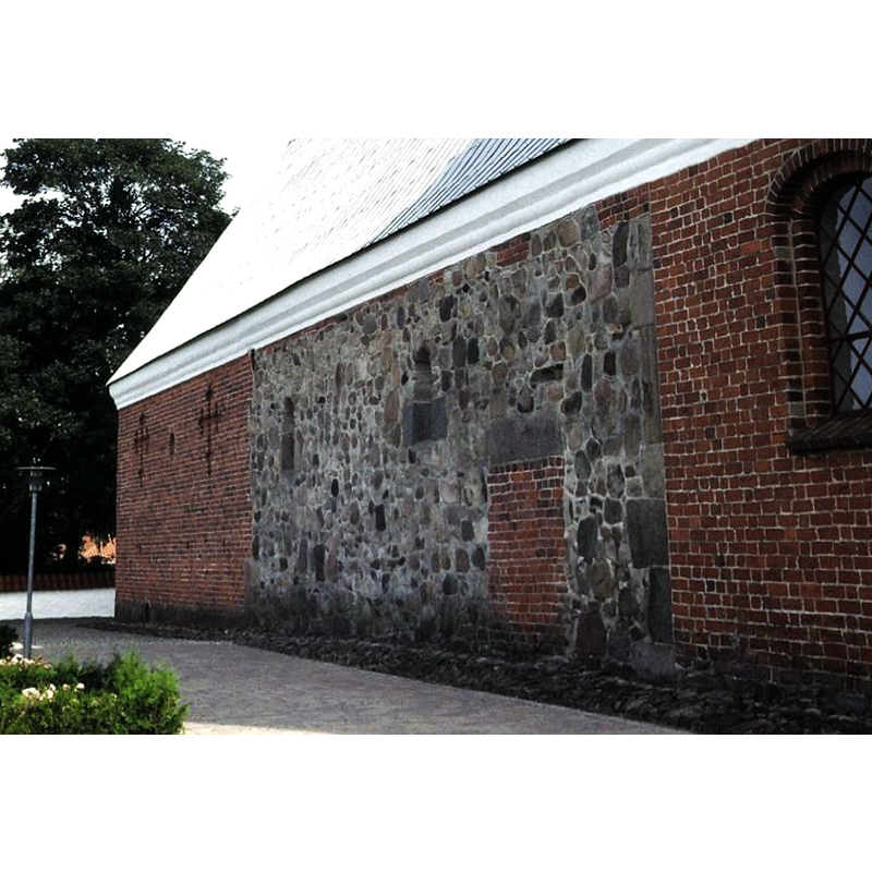 Source caption: "Hornslet Kirke i Danmark. Skibet set fra nord" [NB: part of the north wall of the medieval church has been retained; most of the stones show as undressed split boulders and rubble, with some dressed stone lintels and corner stones]