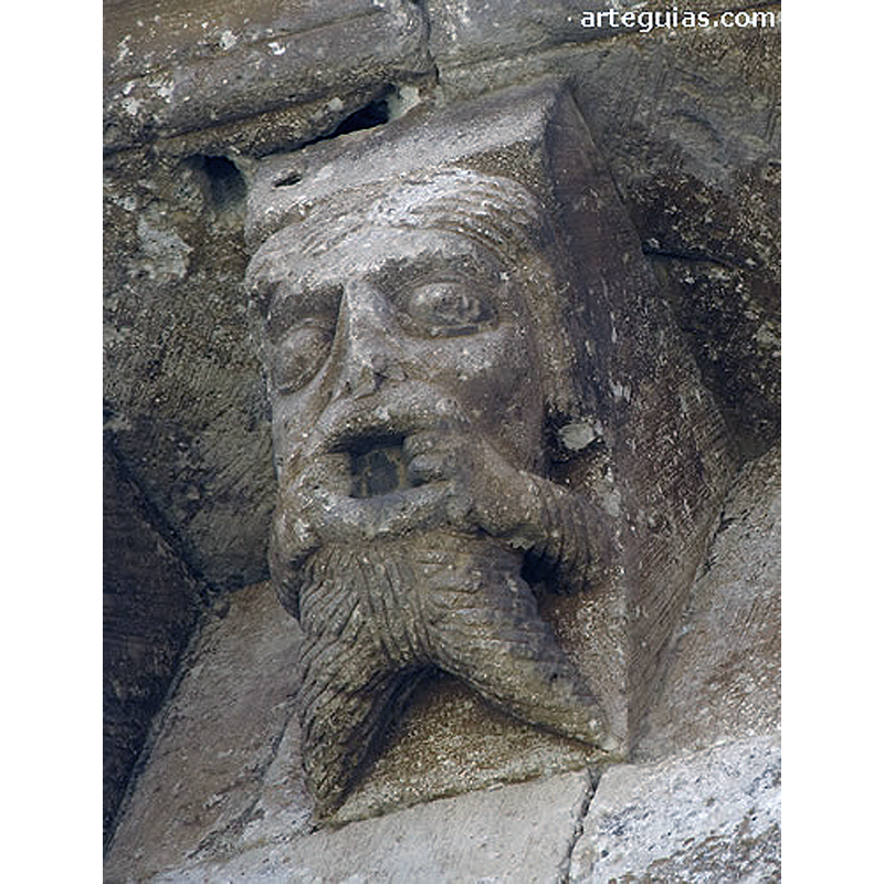 Source caption: "La colección de canecillos de esta iglesia de Arlanzón es muy original y expresiva, además de conservarse muy bien. Entre los figurados podemos destacar una cabeza humana con barba separada en dos picos, que estira su boca por las comisuras labiales valiéndose de las manos"