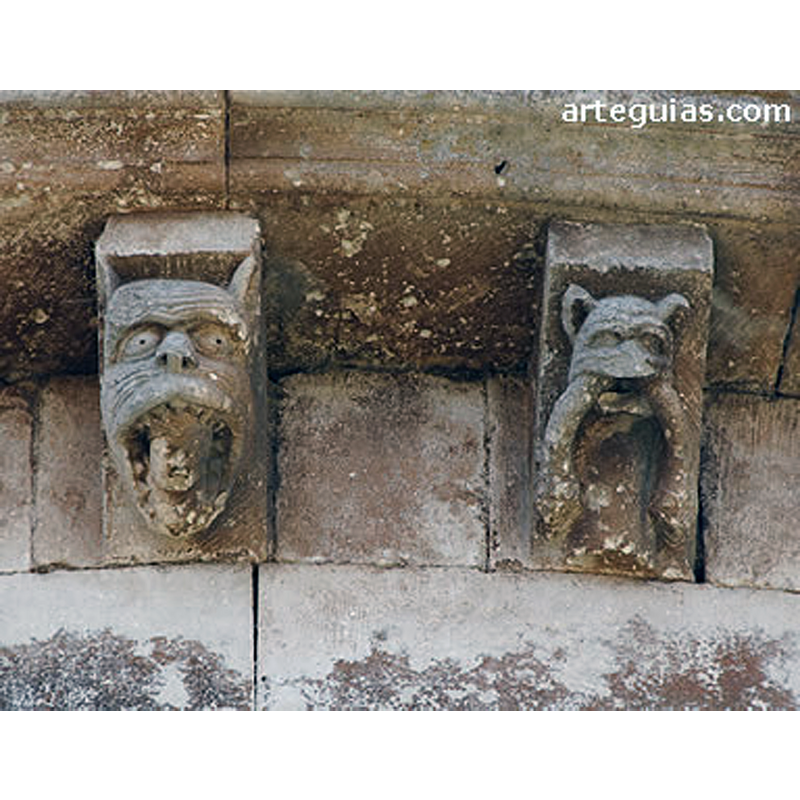 Source caption: "La colección de canecillos de esta iglesia de Arlanzón es muy original y expresiva, además de conservarse muy bien [...] Una pareja de canecillos muestra una iconografía relacionada El de la izquierda es una cabeza animal que tiene entre sus fauces un ser humano, mientras que el de la derecha muestra otra bestia de cuya boca cuelgan dos serpientes."