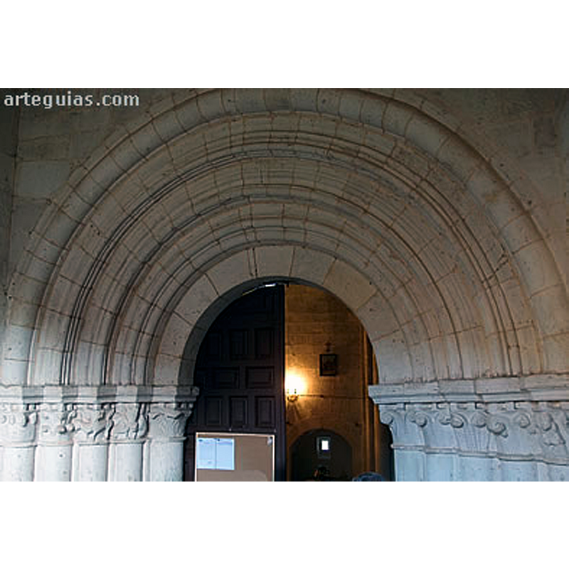 Source caption: "Detrás de una puerta que parece remontada en el muro norte aparece la auténtica portada de la iglesia, de apreciables dimensiones y categoría, muy similar a la de Pineda de la Sierra por sus gruesas columnas. Algunos de los capiteles son historiados."