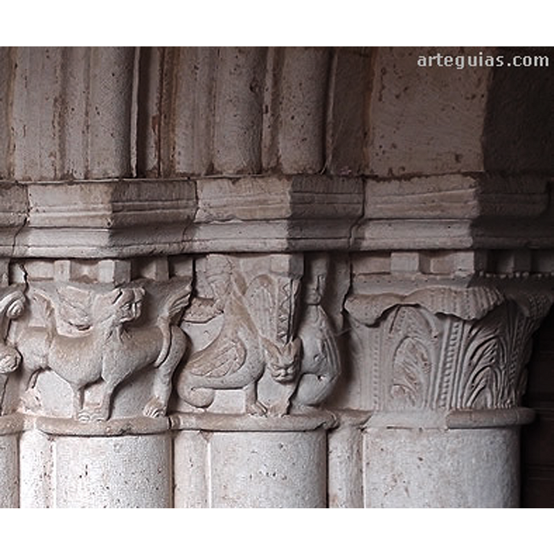 Source caption: "Detrás de una puerta que parece remontada en el muro norte aparece la auténtica portada de la iglesia, de apreciables dimensiones y categoría, muy similar a la de Pineda de la Sierra por sus gruesas columnas. Algunos de los capiteles son historiados."