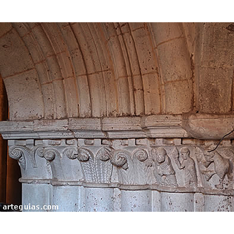 Source caption: "Detrás de una puerta que parece remontada en el muro norte aparece la auténtica portada de la iglesia, de apreciables dimensiones y categoría, muy similar a la de Pineda de la Sierra por sus gruesas columnas. Algunos de los capiteles son historiados."