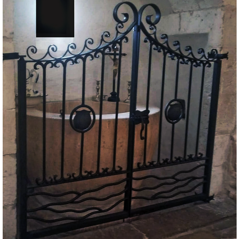 Source caption: "Puerta forjada artesanal diseñada en nuestro taller para la pila bautismal de la Iglesia de Arlanzon"