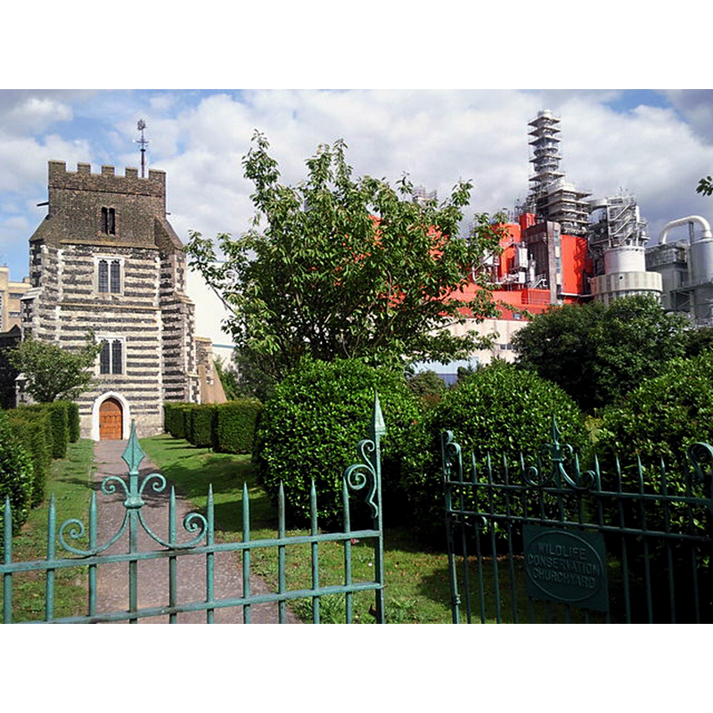 Source caption: "The churchyard of St Clement's, West Thurrock is now a nature reserve as can be seen on the sign on the gate. The church featured in the film Four Weddings and a Funeral and was possibly chosen as there are no houses anywhere near. Thames-side industry, such as the Procter & Gamble soap works seen here, surrounds the churchyard instead."