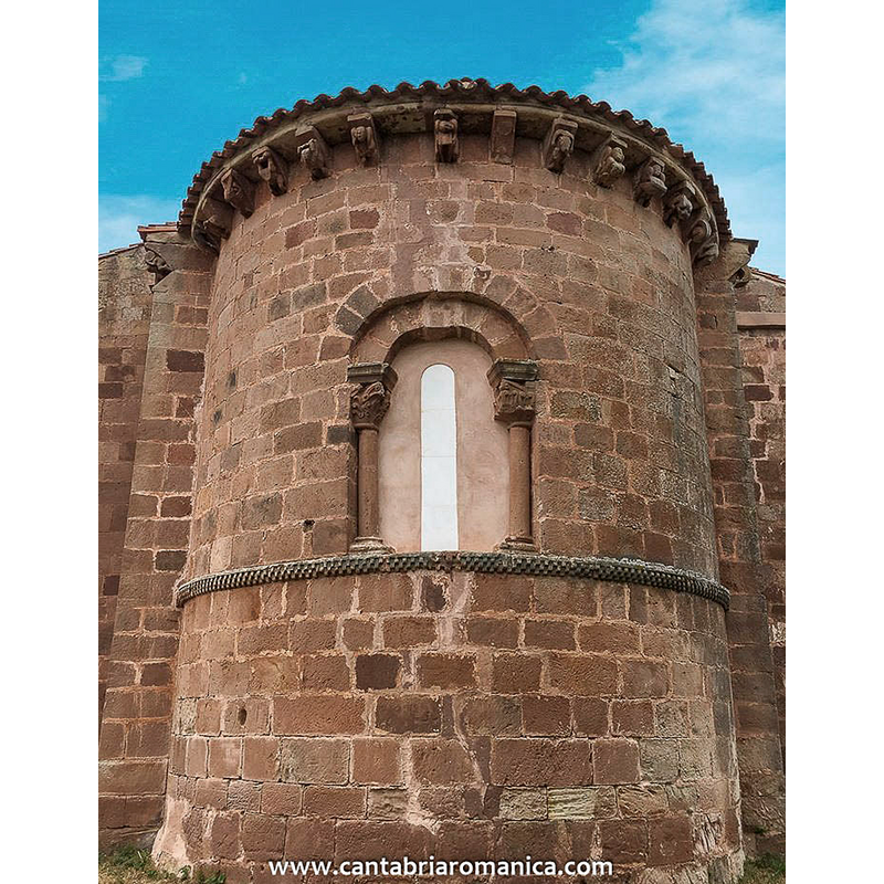 Source caption: "Centrándonos en los elementos plenamente románicos podemos empezar por el ábside que es muy alto, al estilo del de Cervatos, con forma semicircular y que se une directamente al presbiterio sin ningún contrafuerte o columna que lo divida en calles aunque si queda dividido en dos cuerpos por una imposta situada algo más cerca del suelo que de la cornisa, decorada con taqueados en tres filas. Sobre ella se coloca la ventana, también de fábrica plenamente románic,a y que se sitúa en el mismo centro del muro del àbside. Esta ventana queda enmarcada por los lados por dos columnas de fuste liso que están coronadas por capiteles de tema vegetal."
