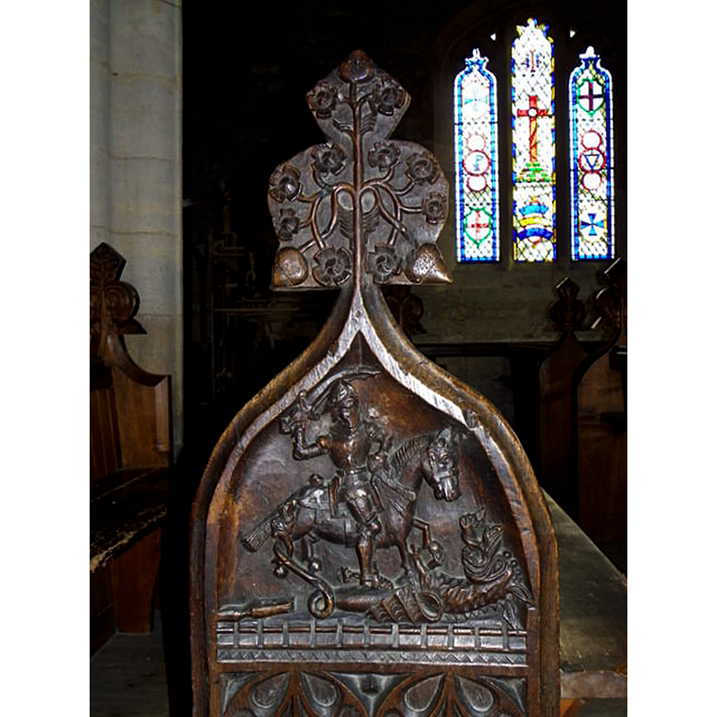 Source caption: "Detail, Church of St Peter and St Paul. The bench ends and poppy-heads are highly decorated. This bench end depicts St George slaying the dragon."