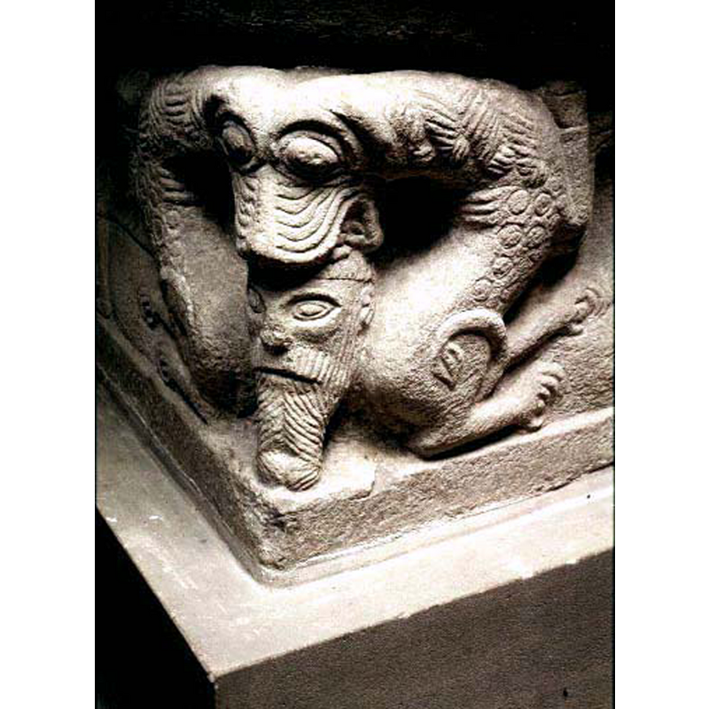 a complicated arrangement: attached to a single lion head are two bodies of rampant-regardant lions; the single head holds in its jaws the head of a bearded man; thsi carving is on the opposite angle across from the ram's head