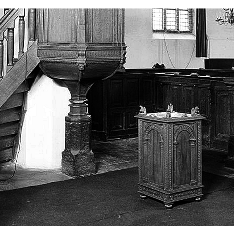 Source caption: "Nederlands Hervormde Kerk: preekstoel en doopvont" -- the stone support of the 1610 wooden pulpit may be the former base of a baptismal font [cf. FontNotes]; the wooden quadrangular object on the ground in front of the pulpit is probably the modern baptismal font
