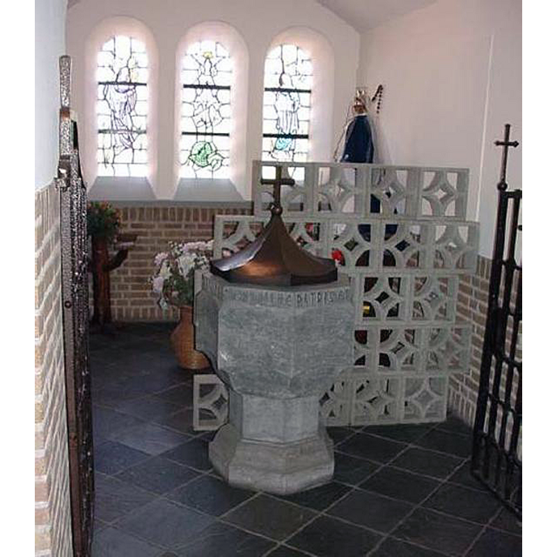 Source caption: "Doopvont, hardsteen. Zevenhoekige voet, stam en cuppa met holzwenkende vlakken. De vont bestaat uit twee delen, waaronder een heilig putje. Langs de bovenrand van de cuppa staat de tekst: EGO TE / BAPTIZO / IN NOMINE / PATRIS ET / FILII ET / SPIRITUS / SANCTI. De vont is gedekt met een zevenhoekige holzwenkend koperen deksel, gekroond door een kruis. De doopvont staat nog steeds in de doopkapel, maar is verplaatst. De aansluiting van het heilig putje is nog in de grond te zien, maar is afgesloten" -- the modern font