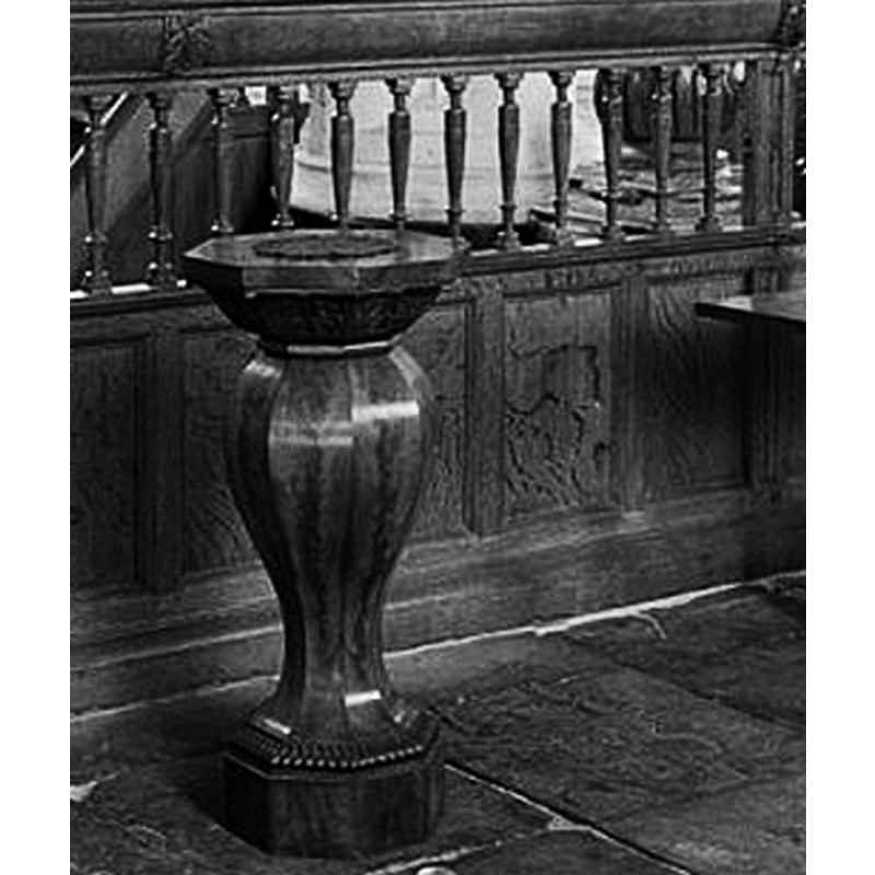 the wooden font in the foreground; the stone base of the pulpit, the former base of a baptismal font, is partially visible behind the railing
