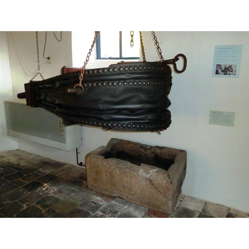 Source caption: "Blaasbalg en blusbak (vroeger doopvont uit de kerk) uit de smederij van Niehove in de kerk van Niehove." -- the set-up now inside the church replicates the environment in which this large stone object, claimed to be an old baptismal font, served as cooling vat in the forge of Noehove