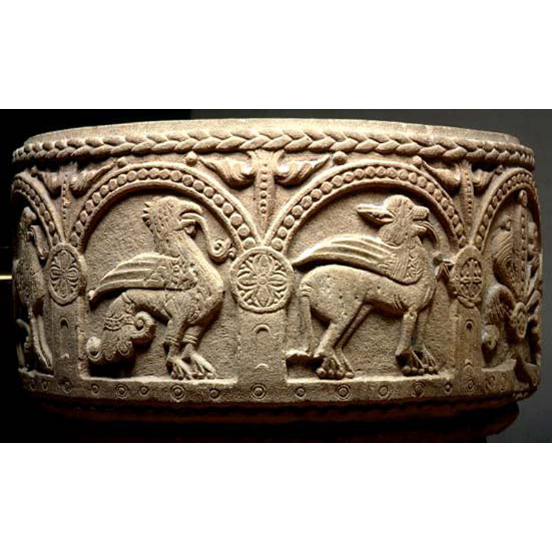 very stylised capitals, round, with inscribed large quatrefoiled motifs; each column has a round window inscribed on it