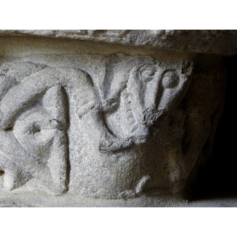 X-shaped, like the one on the other side of the base; being held and bitten by the animal (dragon?) on its right