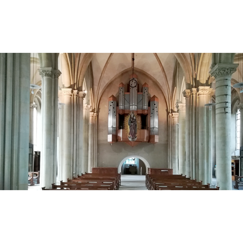 Source caption: "St. Johannes der Täufer ist eine katholische Kirche in der Stadt Billerbeck im Bistum Münster und eine der beiden Kirchen der Pfarr- und Propsteigemeinde St. Johannes und St. Ludgerus." -- the baptismal font is located in the tower room, beyond the little arch visible beneath the organ loft