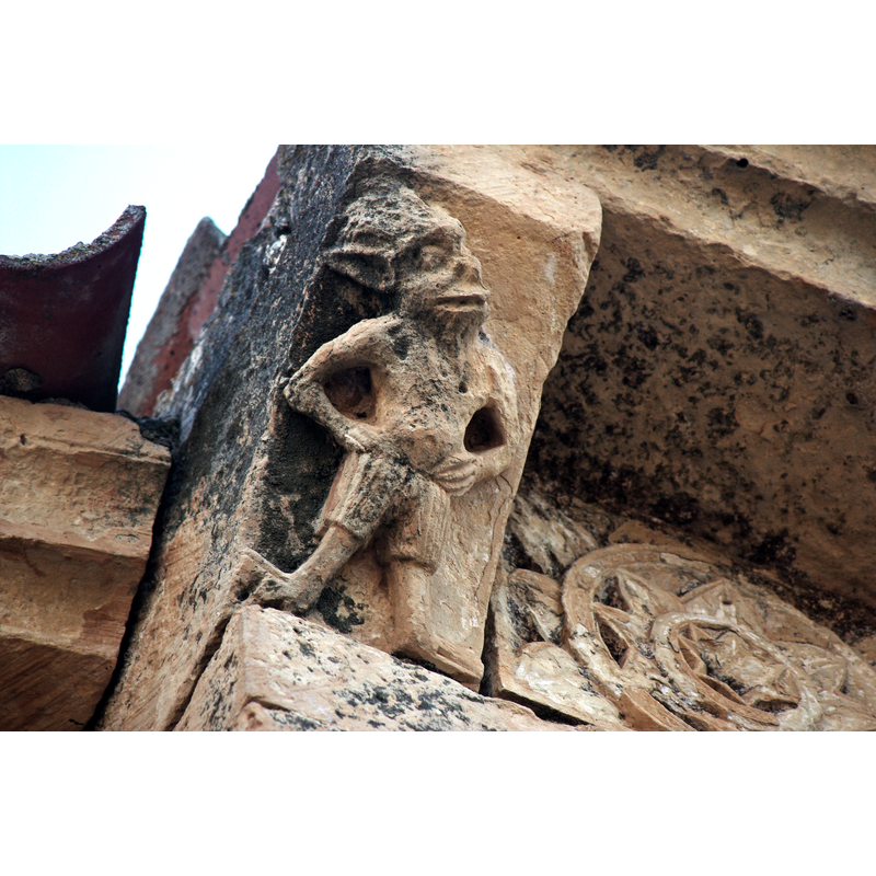 Source caption: "Canecillo del ábside de la iglesia de San Vicente Mártir en Pelayos del Arroyo (Segovia, España)." -- "En la cornisa del muro septentrional del presbiterio encontramos, junto al codillo del ábside, un canecillo decorado con un rudo diablillo antropomorfo de abultado vientre y ataviado con calzas, de grotesco rostro barbado, orejas puntiagudas y cabellera llameante, dispuesto con los brazos en jarras" [source of the Spanish-laguage description: Enciclopedia del románico [www.romanicodigital.com] [accessed 16 July 2022]]