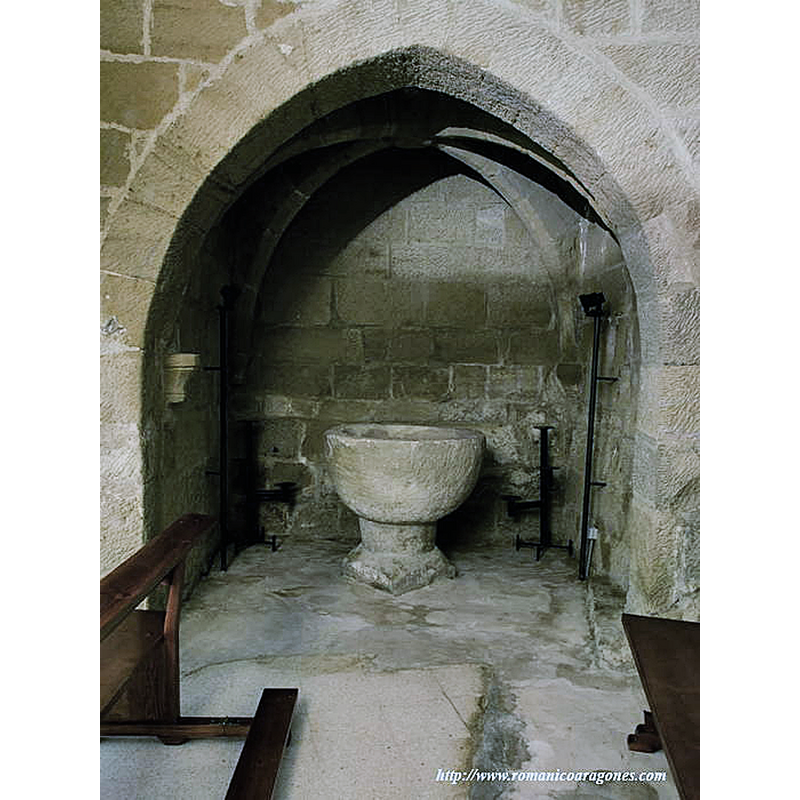 Source caption: "La pila bautismal se halla a los pies junto al muro sur, en una capilla lateral situada bajo el arranque de la torre. Es muy sencilla y probablemente sea la original del templo primitivo"