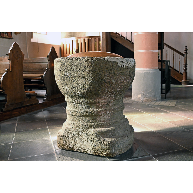 Source caption: " St. Mariä Geburt (Baasem), Taufstein von 1559 aus einem römischen Werkstück" -- the irregularity of the font is obvious in this photograph; ity is quite possible that the flattened side may have been done to fit it against the wall or in a tight spot, not an uncommon fate of some fonts