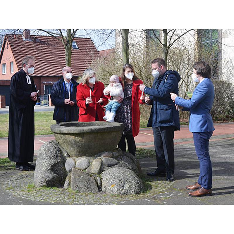 Source caption: "Weitergabe des Osterlichtes am Taufstein vor der Martinskirche: Pastor Rainer Müller-Jödicke (von links), Wolfgang und Gabriela Kasten, Jana, Mila Marie und Benjamin Buske und Diakon Merlin Langrehr.Foto: A. Hessehochgeladen von Oliver Krebs"