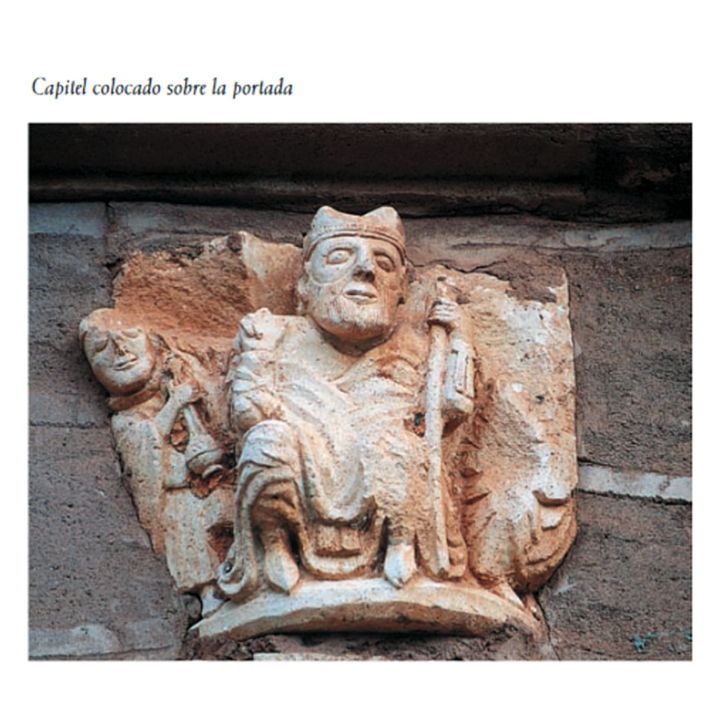 Source caption: "En el muro norte de la nave se encajó la primitiva portada románica [...] Sobre ella se empotró un capitel en el que se representa a un obispo bendiciendo flanqueado por un acólito turiferario y otra figura mutilada [...] Su talla es correcta y su estilo revela la intervención de un taller con buenos recursos plásticos que debió de desarrollar su actividad en torno a 1200"