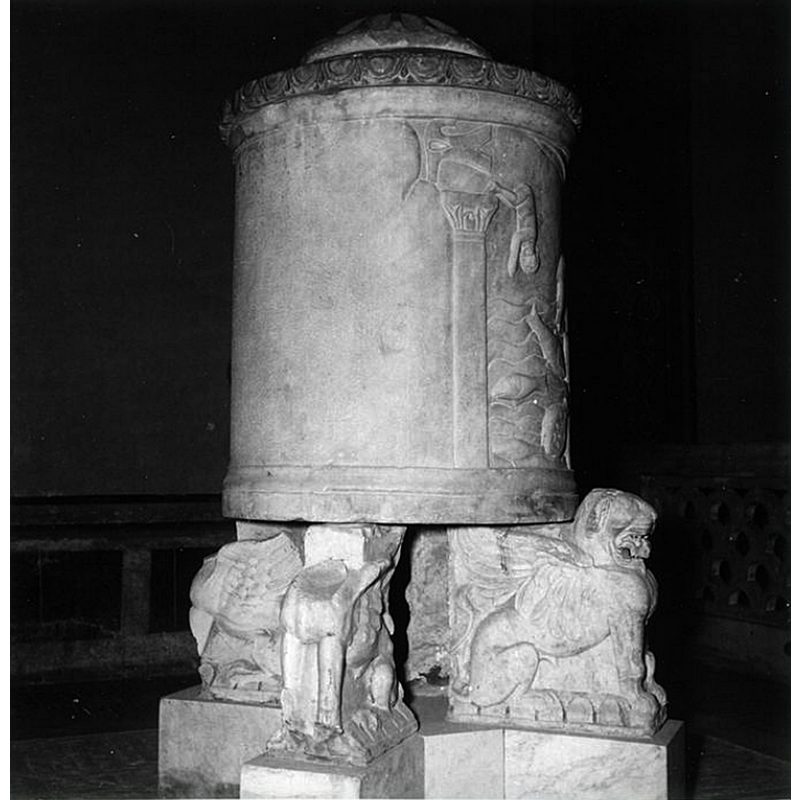 Source caption: "Grottaferrata, S. Nilo abbey, cylindrical baptismal font decorated with fishing scenes, standing on a pedestal (the pedestal has the shape of winged lions)" -- much damaged; they carry the basin on their backs