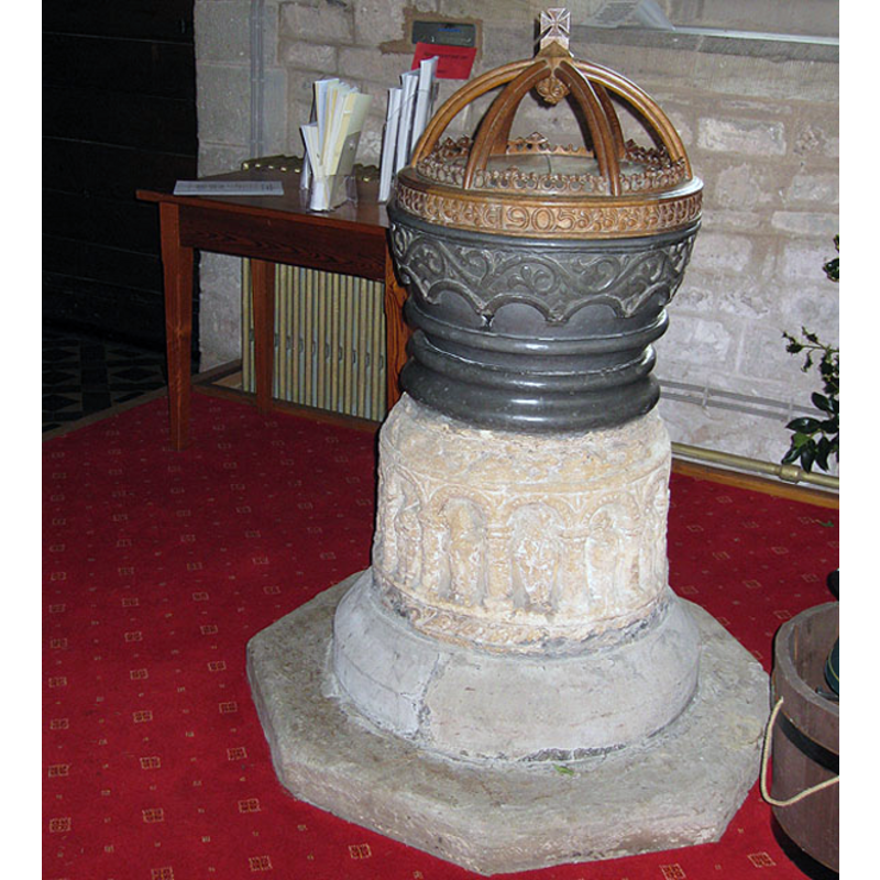 Source caption: "Norman font, St Mary's The stone stem is carved with thirteen arcades which contain images of the twelve apostles and Jesus Christ. When the tower fell in 1810, it crushed the lead baptism bowl, and one made of sandstone was used until the lead one was restored. The wooden lid was carved in 1905."