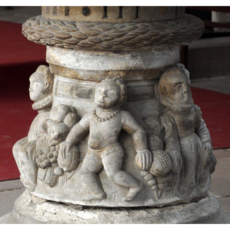two of them on this side of the base: on the left is a seated male in rich clothing; on the right is seated female, also dressed in rich coltes; between them a pracing putto and large piles of fruit