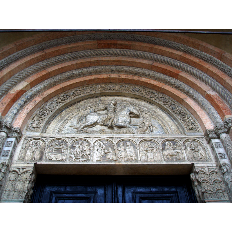 Source caption: "Im Tympanon die Darstellung des Hl. Georg im Kampf mit dem Drachen als Relief, darüber Ornamente mit Tieren und Pflanzen [...] Lunette (showing Saint George) and architrave (showing Scenes from the New Teastament) from the main portal of the Cathedral of Ferrara, sculpted by Romanesque artist "Magister Nicholaus" (12th century)."