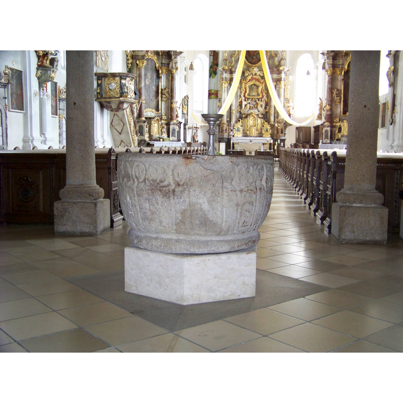Source caption: "Bad Kötzting, Herrenstraße 13. Katholische Pfarrkirche Mariä Himmelfahrt. Saalkirche mit eingezogenem Chor. Großer Taufstein im Mittelgang unter der Empore auf neuem sechskantigen Marmorsockel. Außen an der Schale sind schwach die Umrisse von Personen zu erkennen. Möglicherweise sind Jesus und Johannes der Täufer im Kreis der Apostel bei der Taufe Jesu im Jordan dargestellt."