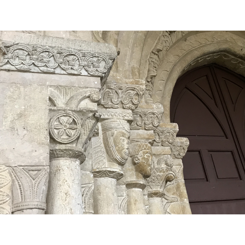 Source caption: "LA PORTADA ES UN BUEN EJEMPLAR DEL SIGLO XIII, SU ARCO APUNTADO VOLTEA SOBRE CUATRO COLUMNAS A CADA LADO. LAS ARQUIVOLTAS SE DECORAN CON: BAQUETONES FESTONEADOS, HOJAS DE ACANTO, BAQUETONES LISOS, DIENTES DE SIERRA, ROSETAS GEOMÉTRICAS. LOS CAPITELES DE LAS COLUMNAS MUESTRAN ORNAMENTACIÓN MUY VARIADA CON FORMAS TRONCOPIRAMIDALES, ROSTRO DE UNA DAMA CON TOCA DE BARBUQUEJO, SERES MONSTRUOSOS EN LUCHA CON ALAS Y FUERTES GARRAS, UN ÁGUILA EN PRESA SOBRE UN CONEJO Y DOS PALOMAS QUE, ENFRENTADAS BEBEN AGUA DE UNA COPA"