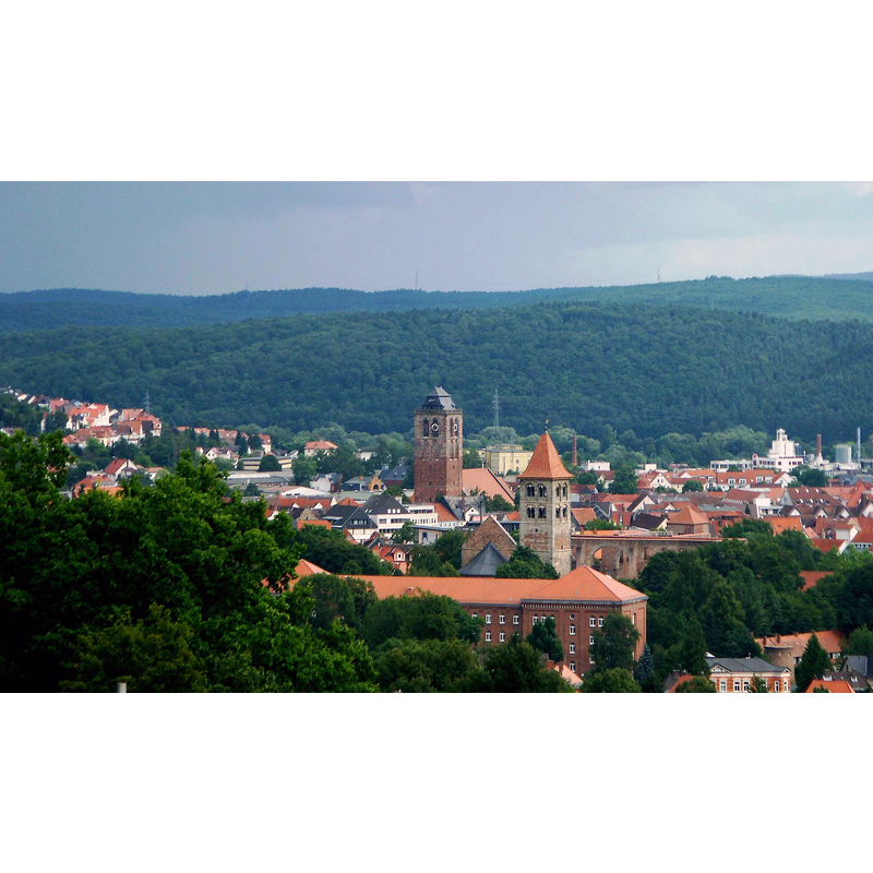 Source caption: "Blick über die Altstadt von Bad Hersfeld aufgenommen vom Tageberg. Im Vordergrund ist das ehemalige Kasernengebäude (heute Finanzamt) von 1870 zu sehen, dahinter Stiftsruine und im Hintergrund der Turm der Stadtkirche, er ist das Wahrzeichen von Bad Hersfeld. Im Hintergrund erhebt sich der Seulingswald." -- the tower in the foreground is Katharinenturm; behind it, and to the left, is the tower of the Stadtkirche