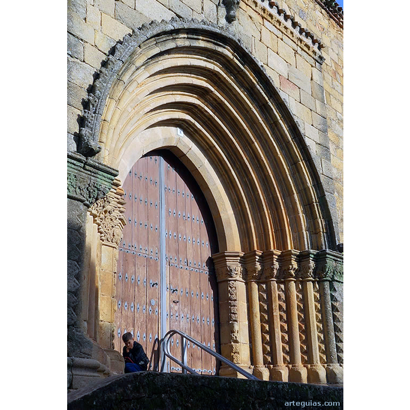 Source caption: "Pero lo que le ha aportado notoriedad al templo es, sobre todo, su puerta meridional pues se suele considerar tardorrománica del siglo XIII. Pero incluso si fuese de una época tan avanzada como el siglo XV sería evidente una gran arcaización de la estructura arquitectónica y de la escultura que nos llevaría a pensar en una inspiración (o incluso imitación) de modelos más antiguos, como la puerta occidental de la Catedral Vieja de Plasencia."