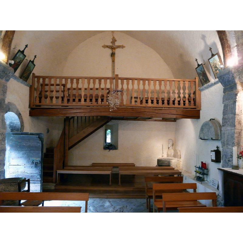 Source caption: "Nef et tribune de l'église Saint-Barthélémy, Bramevaque, Hautes-Pyrénées, France." -- showing the holy-water stoup by the entranceway, bottom-left corner of the image, and the baptismal font, in the north-west corner of the nave, beneath the gallery -- also shown is the detached tympanum seen here on the wall, right side of the image