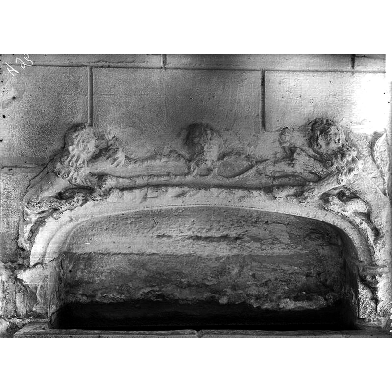Source caption: "Enfeu servant de bénitier. Cuve rectangulaire, creusée aux deux tiers dans la maçonnerie du mur Sud de l'église et surmontée d'une sorte d'enfeu dont l'archivolte est tracée en anse de panier et retombe sur deux petits culots moulurés."
