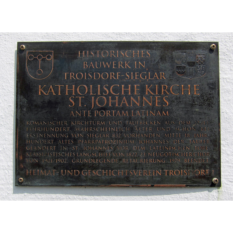 Source caption: "plaque describing the construction phases of the St. Johannes church in Sieglar, Germany" -- it mentions the medieval font and the change in dedication of the church between the two St. Johns
