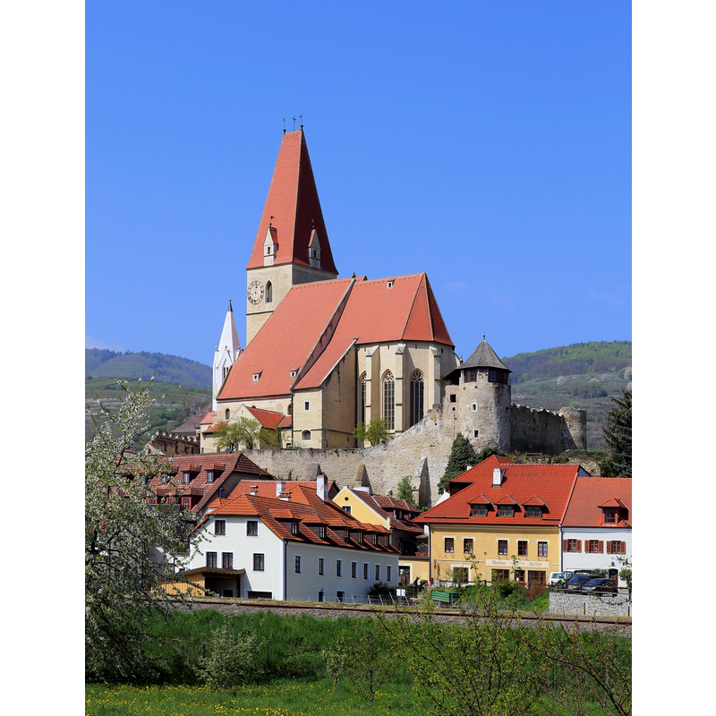Source caption: "Südostansicht der römisch-katholischen Pfarrkirche Mariae Himmelfahrt in der niederösterreichischen Marktgemeinde Weißenkirchen in der Wachau. Die dominierend den Ort überragende Pfarrkirche ist ein wuchtiger, vielteiliger Bau, der in mehreren Bauphasen zwischen dem 13. und 18. Jahrhundert errichtet wurde und von einer turmbewehrten Befestigungsanlage umgeben ist. Der spätgotische Chor wurde von 1519 bis 1526 errichtet und der mächtigte Nordwestturm 1502. Der kleinere Turm - südlich in der Westfront leicht eingestellte - ist der ursprüngliche Turm der zweischiffige Vorgängerkirche und wurde um 1330 errichtet."