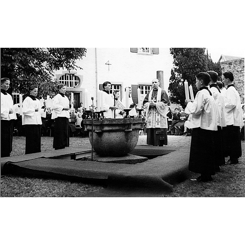 Source caption: "Das Theaterstück "Die Berufung"	 wurde am 19.08.1962 zum 40. Priesterjubiläum von Pastor Hans Wichert im Quadrum aufgeführt. In der Mitte der noch nicht restaurierte Taufstein, der jetzt unter dem Turm in der Kirche steht." [NB: the medieval basin from Friesdorf seen here in Oberpleis, before its restoration and installation inside the church]