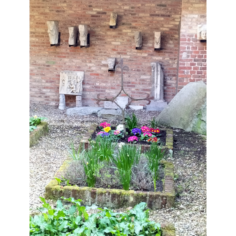 two fragments of the font base is discernible at the far back, above the flowers, left of the metal cross