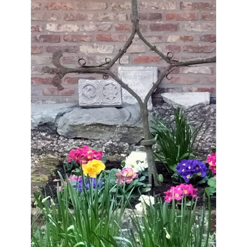 two fragments of the font base is discernible at the far back, above the flowers, left of the metal cross