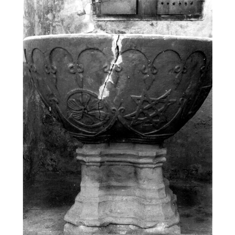 Source caption: "Vista frontal de una pila bautismal de estilo gótico, con pie moldurado al igual que los basamentos de las columnas. La copa lleva al borde un festoneado con lises estilizadas colgantes de las uniones de los arcos; por debajo, otros arcos más amplios proyectan las luses hacia arriba. En medio quedan rosetas y estrellas entrelazadas enmarcadas en círculos o cuadrados. Pila bautismal de la iglesia de San Cristóbal de Heredia".
