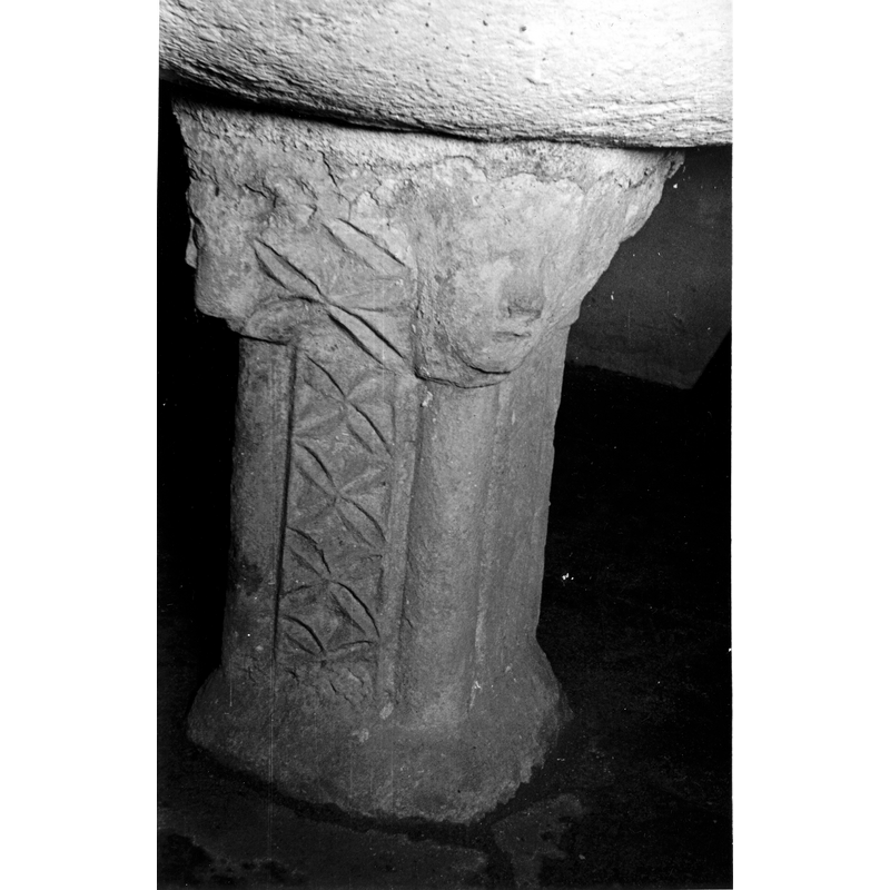 Source caption: "pila bautismal de la iglesia de la Santísima Trinidad de Urturi. Detalle del pie de la pila bautismal; está decorado con bandas incisas verticales y muestra cuatro rostros en los vértices superiores"