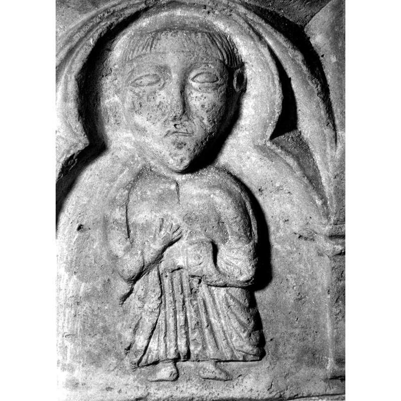 Source caption: "Detalle de una de las figuras de la parte superior de la pila bautismal gótica; se representa una figura de hombre, un apóstol, profeta o fraile franciscan o con un libro en las manos, entre arquerías polilobuladas [...] pila bautismal de la iglesia de la Natividad de Hueto Arriba"