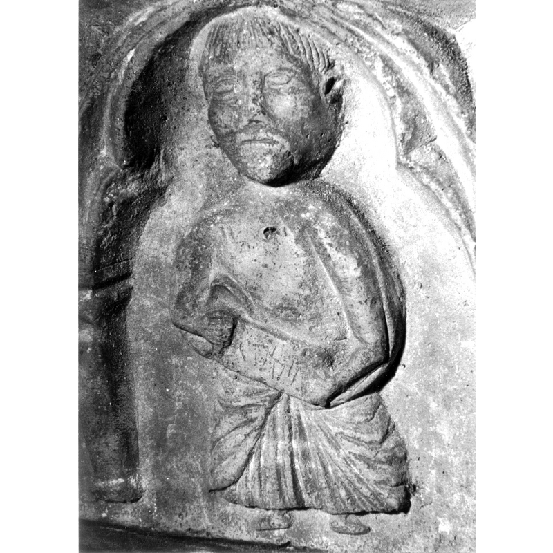 Source caption: "Detalle de una de las figuras de la parte superior de la pila bautismal gótica; se representa una figura de hombre, un apóstol, profeta o fraile franciscano con una cartela en las manos, entre arquerías polilobuladas [...] pila bautismal de la iglesia de la Natividad de Hueto Arriba"